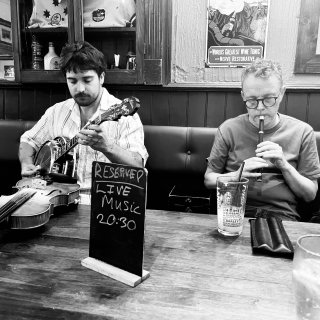 A man playing banjo next to a man playing tin whistle at a pub table.