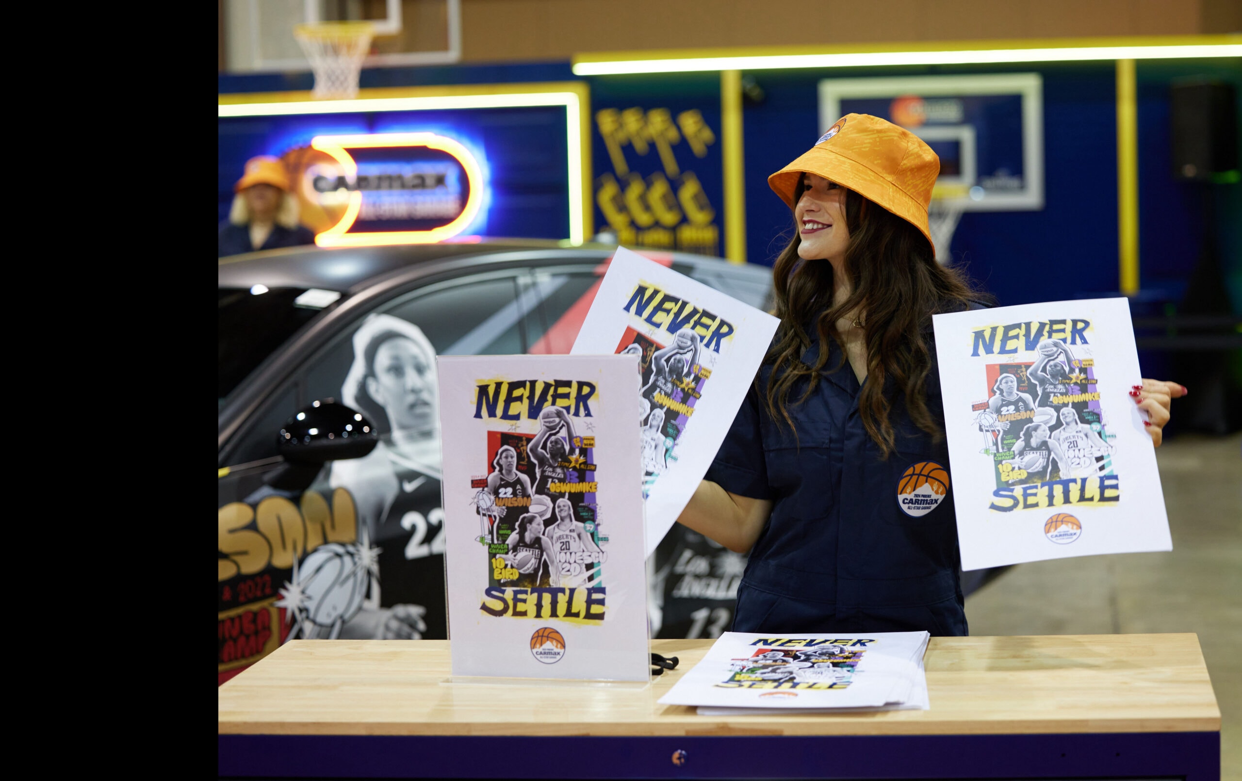 Image of person holding CarMax poster with several WNBA players. CarMax Logo.