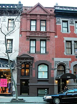 a three-story red brick residential building with dark lower accents sandwiched between two other three-story buildings