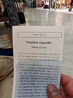 Person holding a small printed French short story booklet titled “Première cigarette” in a public space