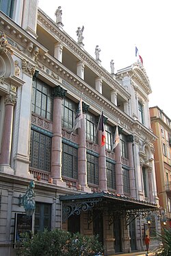 Vue d'un bâtiment de style italien du XVIIIe siècle à colonnes et grandes baies vitrées et statues sur son toit plat.