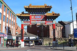 A red gold and blue Chinese arch over a busy city centre street