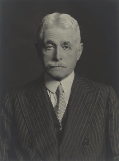 Portrait of a man in early old age, with white hair and a moustache, wearing a formal pinstriped suit.
