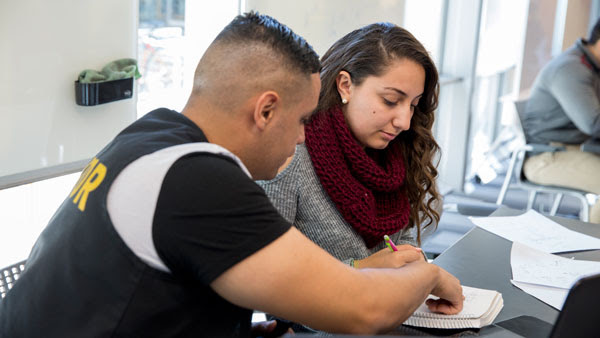 A tutor helps a woman with her classwork at a table in the tutoring center