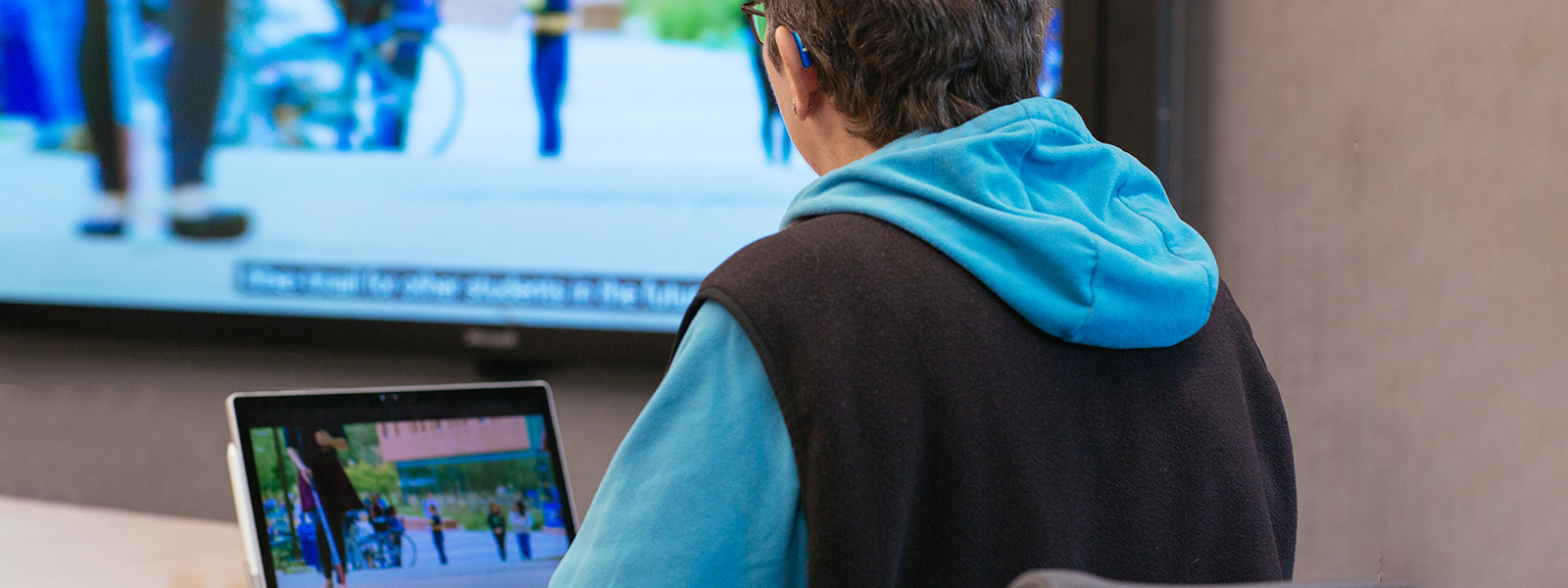 a. A woman who uses a hearing aid, watches a video presentation with subtitles
