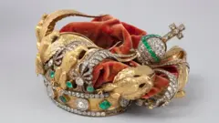 La corona de la emperatriz francesa Eugenia: una corona de oro con diamantes, esmeraldas y águilas doradas, cubierta de terciopelo rojo. Sus decoraciones se pueden ver aplastadas hacia dentro.