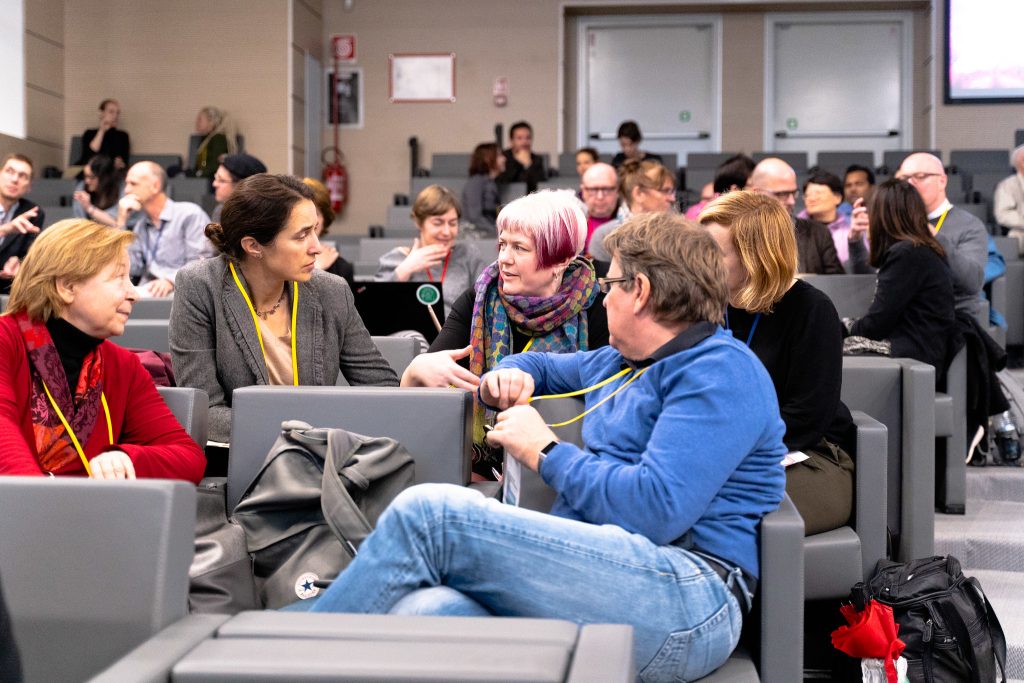 A group of people discussing something, sitting on chairs of an auditorium.