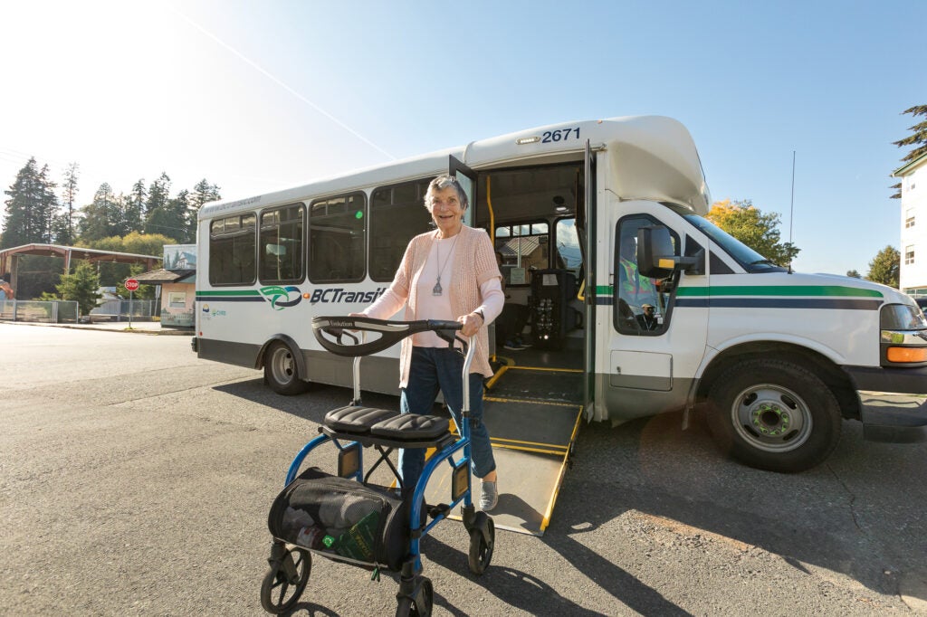 An elderly woman using a walker steps off a transit bus.