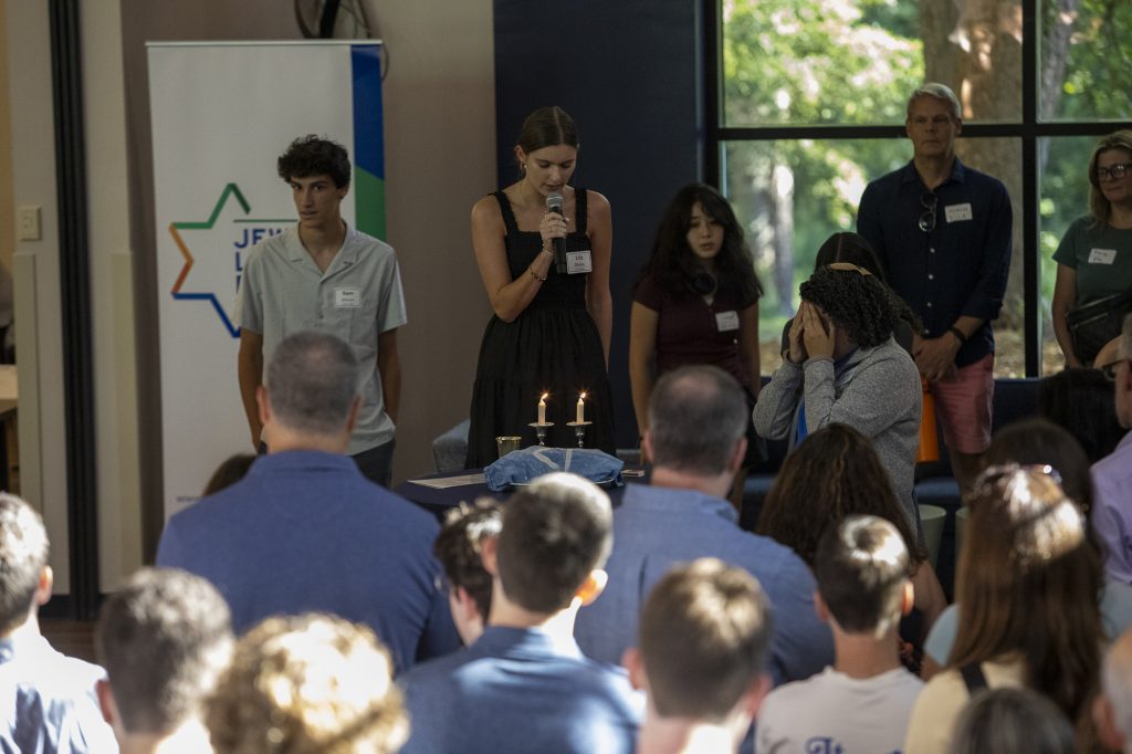 Group gathered at a Duke Shabbat dinner event as a student speaks into a microphone beside lit candles.