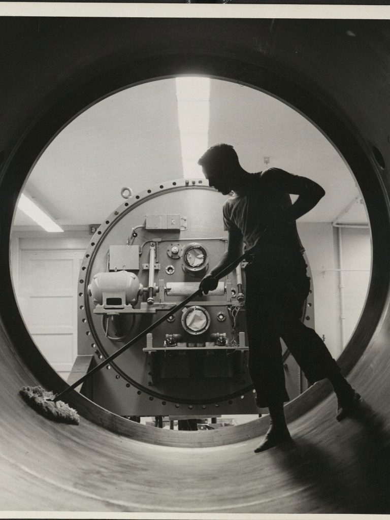 Black-and-white photo of a person sweeping inside a large circular chamber in a nuclear lab.