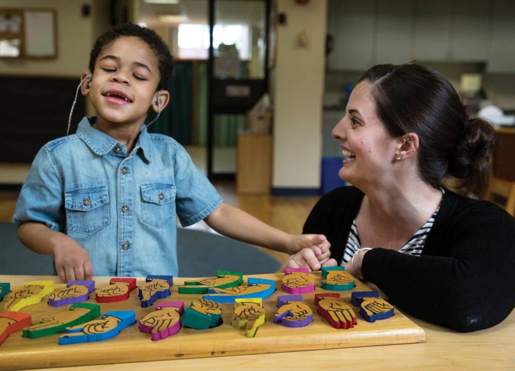 A student playing with a puzzle in a classroom while his instructor looks on