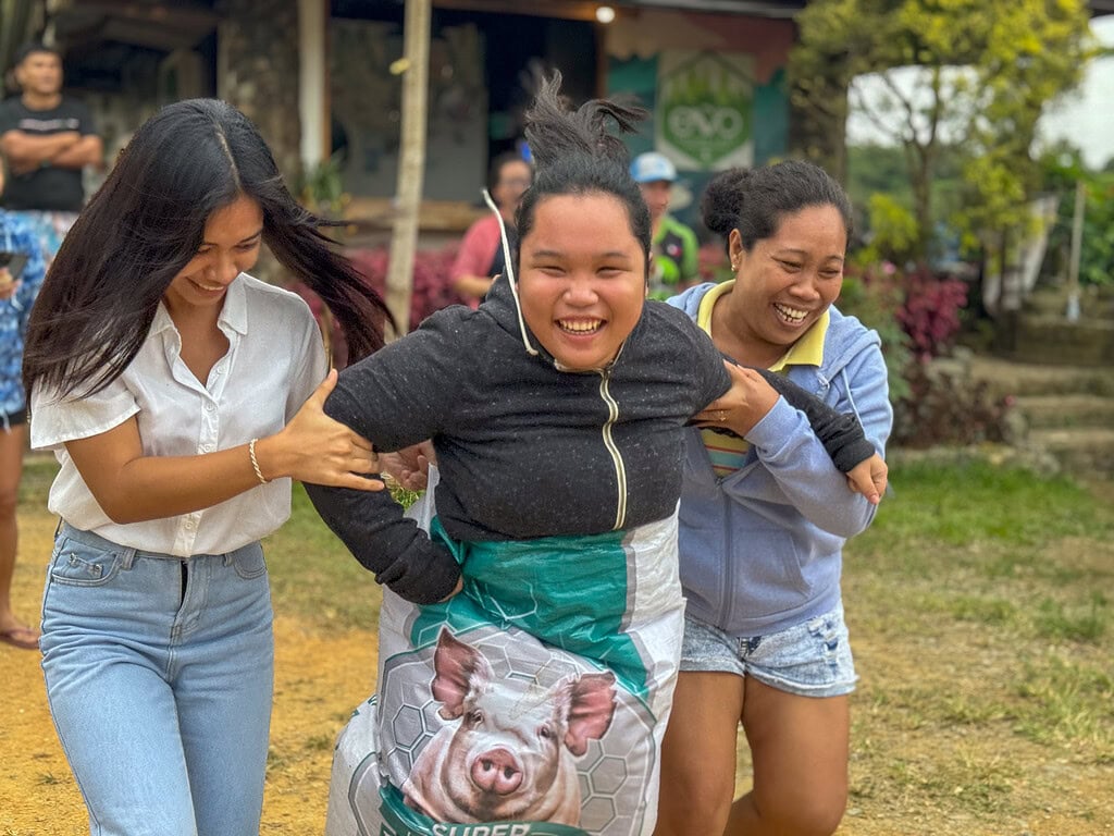 Three girls hold on tight to each other while they hop to the finish line in a sack race.