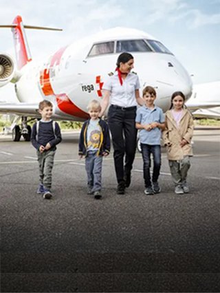Eine Rega-Mitarbeiterin geht mit einer Gruppe von Kindern auf dem Rollfeld an einem Ambulanzjet vorbei.