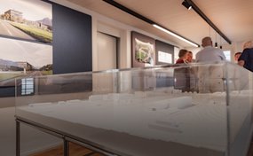 Einblick in das helle Informationsbüro der Rega in Sarnen mit einem weissen Architekturmodell im Vordergrund und Besuchern im Hintergrund.