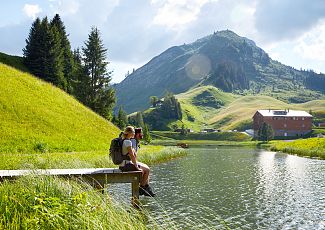Ein Paar sitzt entspannt auf dem Steg am Seebachsee, mit dem glitzernden Wasser im Hintergrund.